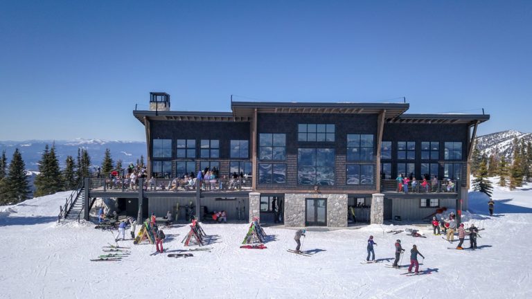 group of skiers in winter on top of Schweitzer Mountain in front of Red Hawk Cafe mountaintop restaurant bar in SkyHouse