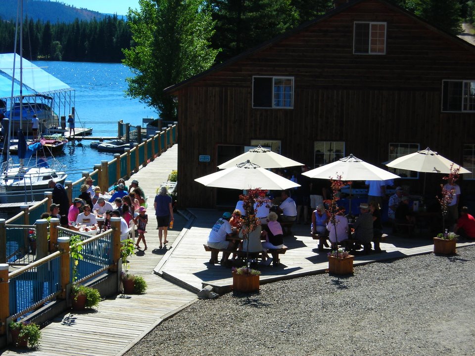 group of people eating on a sunny day deck patio with tan umbrellas lakeside by boat docks at the Blue Diamond Marina Resort
