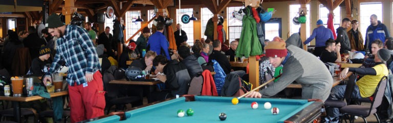 Group of skiers and snowboarders eating, drinking, playing billiards pool at Taps bar pub in Schweitzer Mountain Village