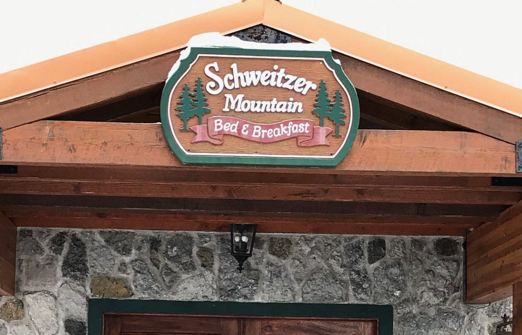Schweitzer mountain bed & breakfast wooden sign front entry with green trees and red ribbon ski in, ski out lodging