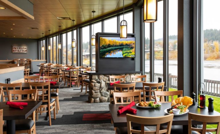 Interior view contemporary design black tables, brown chairs, red napkins, and digital TV screen with windows looking onto the river at Springs restaurant and lounge Kootenai River Inn hotel and casino
